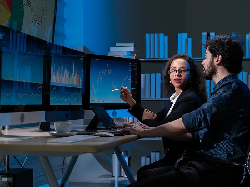 Analysts discussing dashboards on a wall of monitors